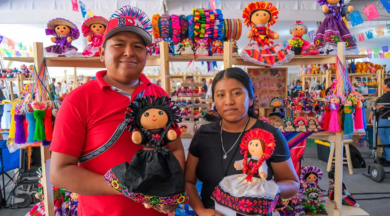 Dos artesanos mostrando sus coloridas muñecas a la venta en la feria artesanal Corazón Artesano. Foto: Cortesía.